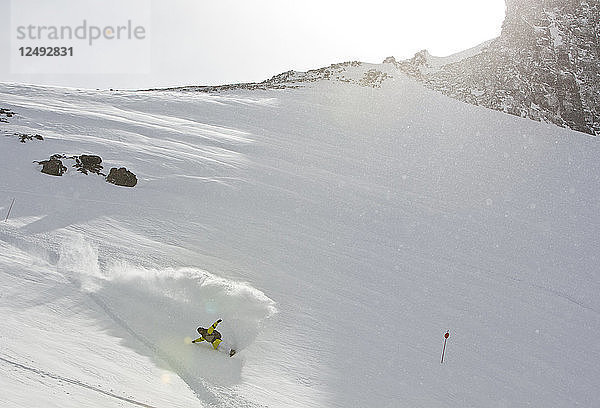 Ein Snowboarder macht einen Powder Turn und spritzt Schnee hoch in die Luft am Cerro Catedral