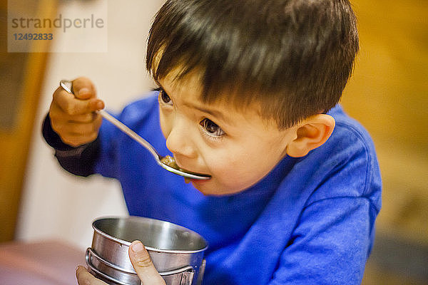 Ein 4 Jahre alter japanisch-amerikanischer Junge isst aus einem Metallbecher.