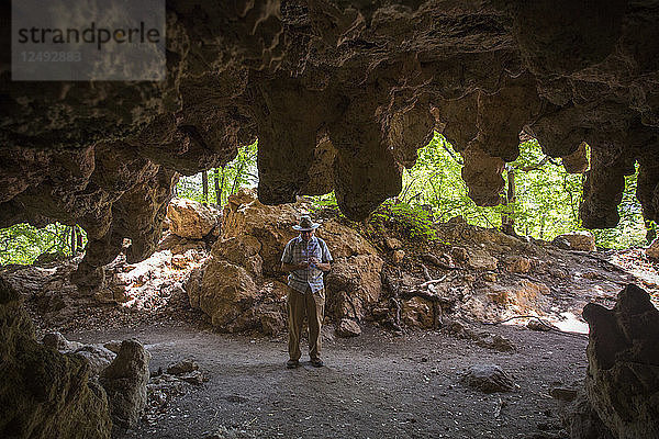 Älterer Herr  der am Eingang einer Höhle mit von der Decke hängenden Stalaktiten steht
