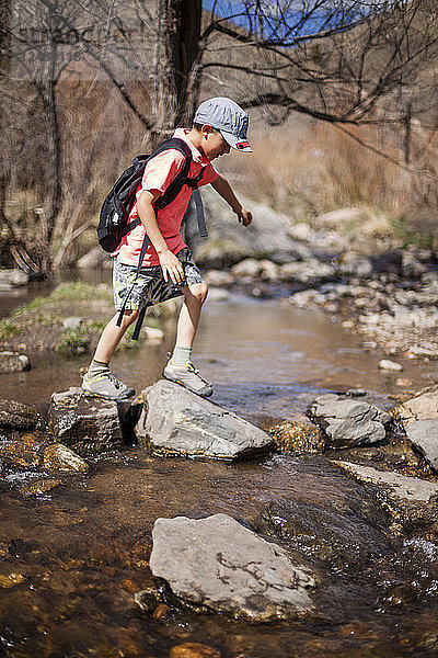 Ein 6-jähriger japanisch-amerikanischer Junge überquert beim Wandern auf dem Hewlett Gulch Trail  Colorado  einen Bach.