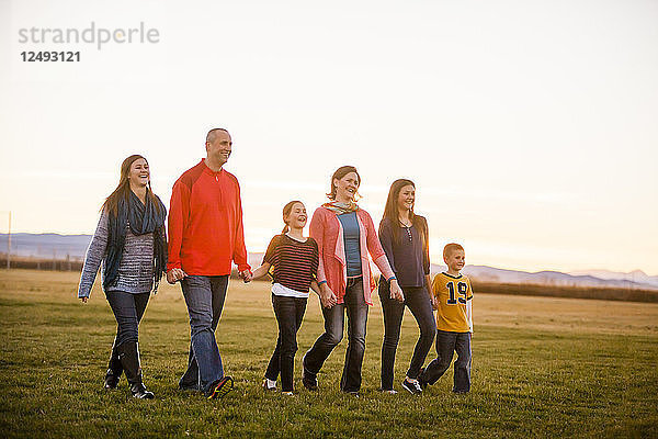 Eine Familie Spaziergang durch ein Feld bei Sonnenuntergang  während die Hände in Bozeman  Montana