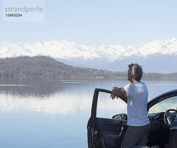 Älterer Mann entspannt sich auf der Tür eines Autos am See