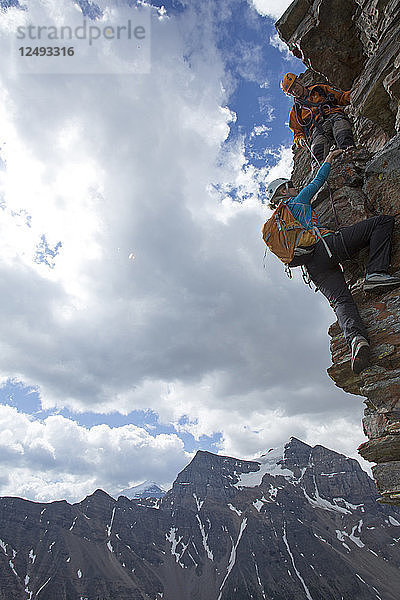 Bergführer hilft einer Bergsteigerin beim Aufstieg über die Felswand