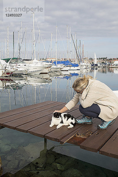 Frau streichelt Katze auf Pier im Hafen