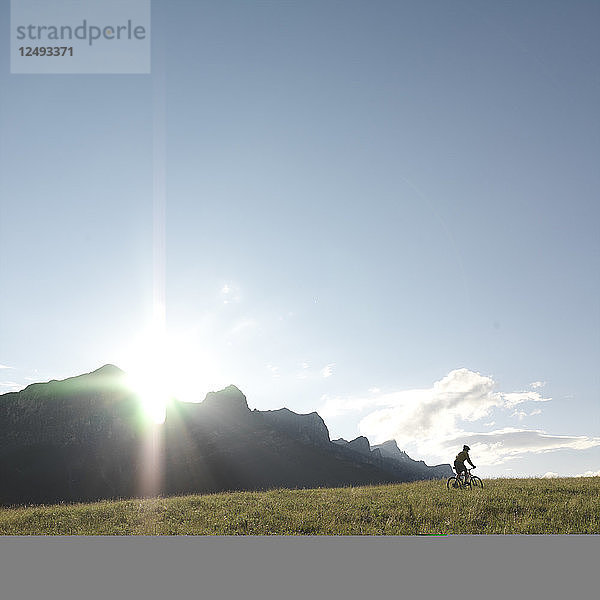 Entfernte Ansicht eines Mountainbikers  der auf dem Kamm einer Wiese fährt