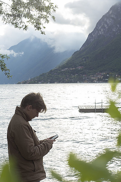 Junger Mann sendet Text am Seeufer und am Steg
