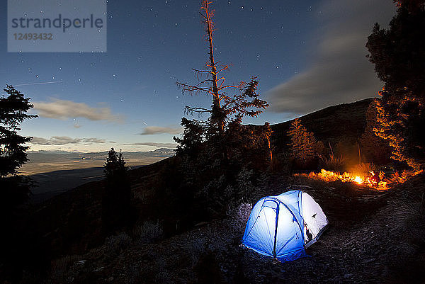 Mann sitzt nachts am Feuer auf seinem Campingplatz.