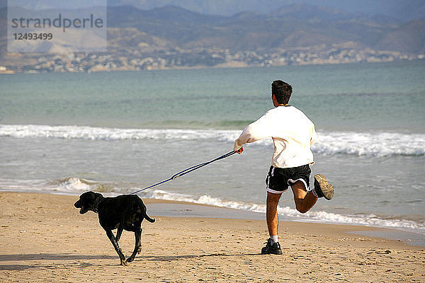 Ein kleiner Junge und sein Hund laufen an einem ruhigen Strand in Aliicante entlang
