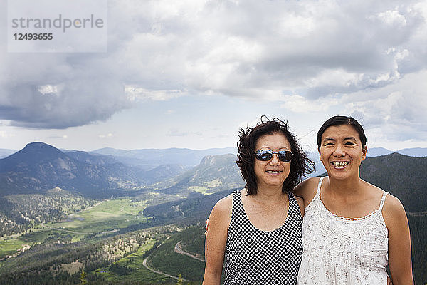 Eine japanisch-amerikanische Mutter und ihre Tochter stehen an der Rainbow Curve Overview  hinter ihnen erstreckt sich der Rocky Mountain National Park.