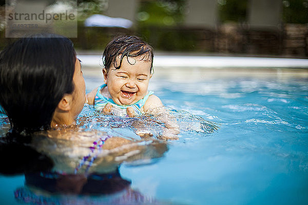 Eine japanisch-amerikanische Mutter schwimmt und hält ihr 10 Monate altes Mädchen in einem Schwimmbad.