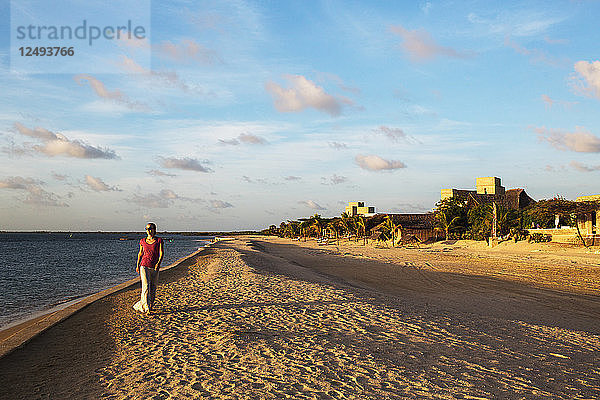 Eine junge Frau spaziert unter strahlend blauem Himmel über den leeren weißen Strand der Insel Manda.