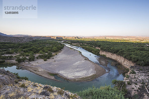 Ein grüner Fluss windet sich um eine tiefe Biegung in einer trockenen Wüstenlandschaft an der Grenze zwischen den USA und Mexiko