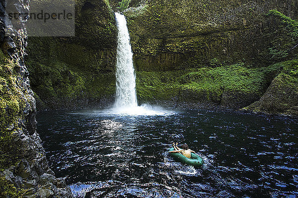 Ein Mann schwimmt in einem Ein-Personen-Rafting in einem dunklen Pool unter einem hohen Wasserfall.