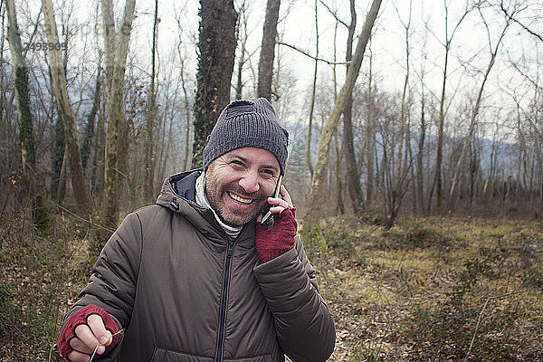 Der glückliche junge Mann  der über das Telefon spricht  während er im Wald spazieren geht