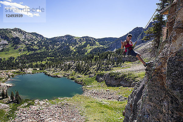 Eine Frau vollendet eine Kletterpartie und gibt das Rock-on-Symbol  während sie in den Wasatch Mountains in Utah wieder auf den Boden abgeseilt wird.