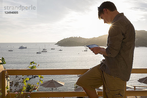 Junger Mann entspannt sich auf der Hotelveranda und benutzt ein digitales Tablet