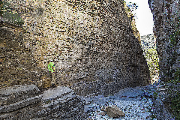 Senior Man Exploring A Narrow Dry Canyon of Steil geschichteten Felswänden