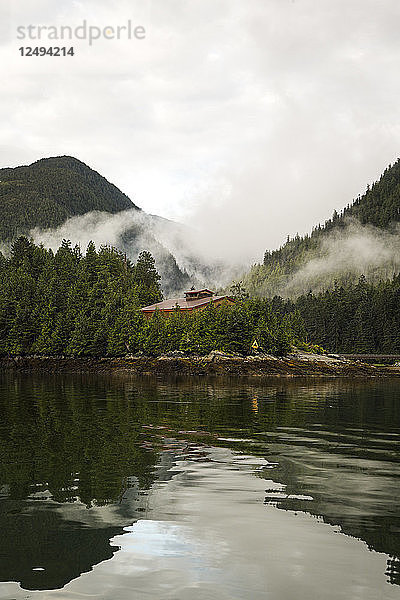 Nebel hängt über einer Dachlinie einer Gemeinschaftshütte in einer dicht bewaldeten Berglandschaft