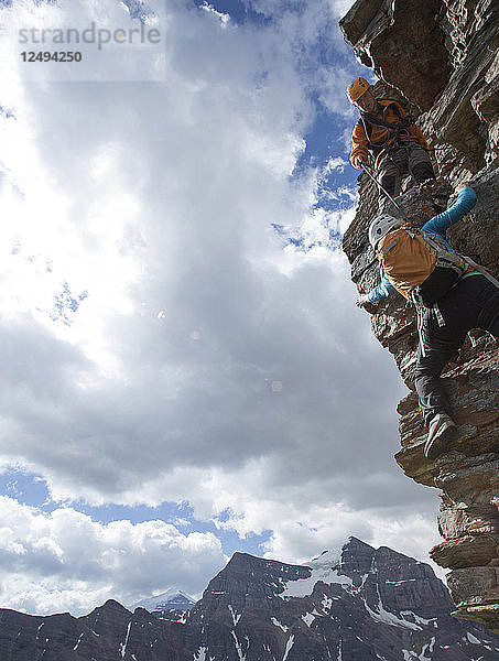 Bergführer hilft einer Bergsteigerin beim Aufstieg über die Felswand