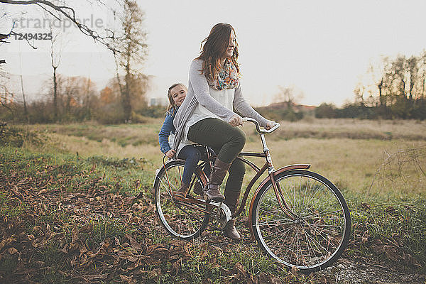 Eine Mutter tritt in die Pedale eines altmodischen Fahrrads  während ihre Tochter auf dem Rücken mitfährt.