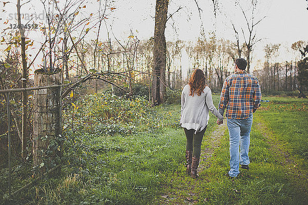 Ein Paar hält sich an den Händen  während es einen alten Feldweg entlanggeht.
