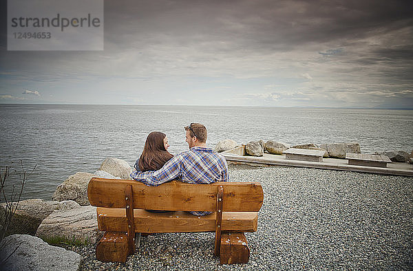 Ein junges Paar sitzt lachend auf einer Holzbank im Robert's Creek Park in der Nähe von Sechelt  BC  Kanada.