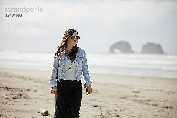 Eine modebewusste Frau spaziert am Rockaway Beach in Oregon entlang.