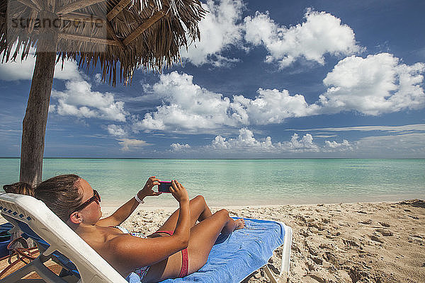 Eine junge Frau macht ein Foto mit ihrem Smartphone  während sie am Strand von Cayo Coco  Kuba  entspannt.