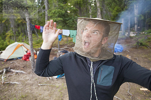 Ein Mann kämpft mit einem Moskitonetz auf seinem Campingplatz gegen Mücken.