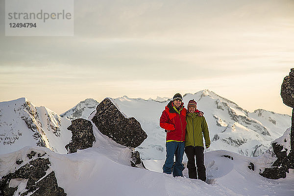 Ein junges Paar posiert für ein Foto auf dem Gipfel eines Berges im letzten Licht des Tages während einer Skitour in den Coast Mountains bei Whistler  British Columbia  Kanada.