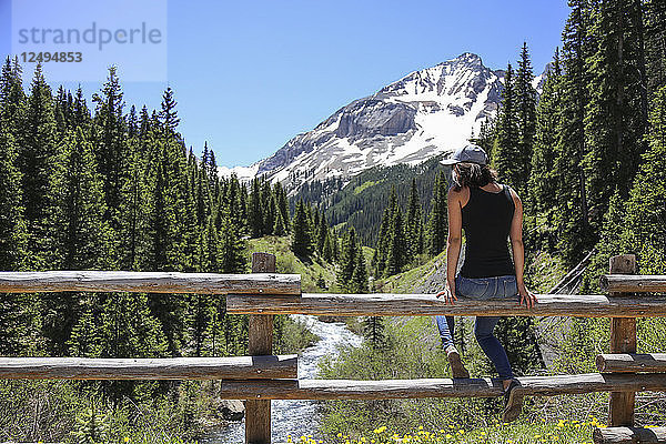 Mädchen sitzend auf Schiene Zaun erforscht Colorado Creek in den San Juan Mountains