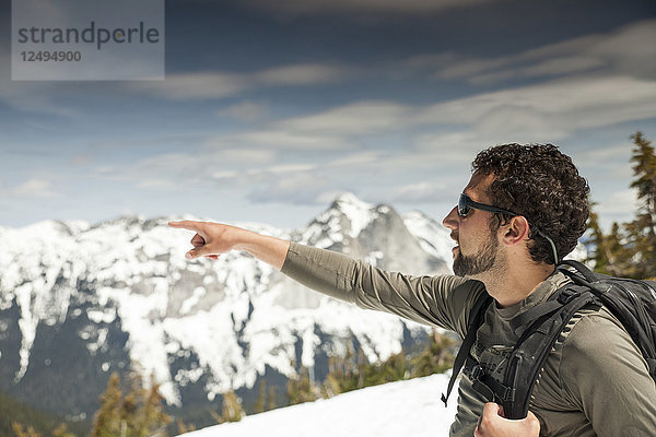 Ein Rucksacktourist zeigt auf eine benachbarte Bergkette  während er auf dem Weg zum Needle Peak ist.