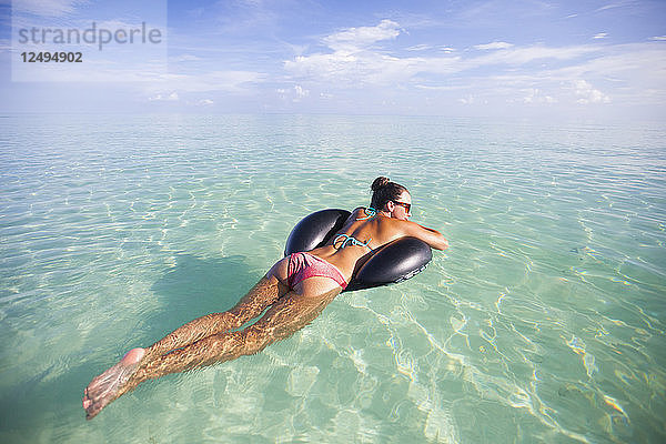 Eine junge Frau schwimmt auf einem aufblasbaren Wasserspielzeug im flachen türkisfarbenen Wasser während ihres Urlaubs in Cayo Coco  Kuba.
