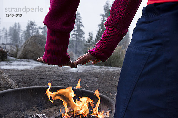 Ein Mädchen wärmt sich an einem Wintertag in Big Bear  CA  die Hände am Feuer.