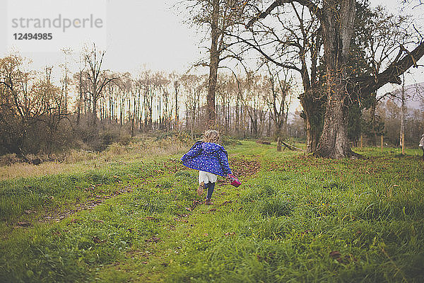 Ein junges Mädchen in einer blauen Jacke läuft durch ein grasbewachsenes Feld.