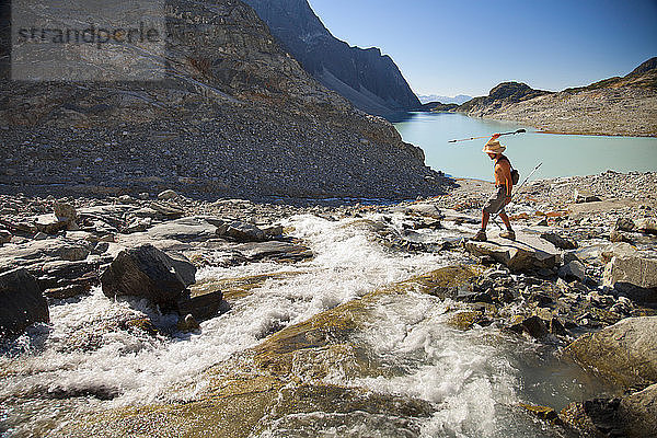 Ein hemdsärmeliger Wanderer versucht  mit einem Trekkingstock im Wedgemount Lake im Garibaldi Provincial Park Fische aus einem Fluss aufzuspießen.