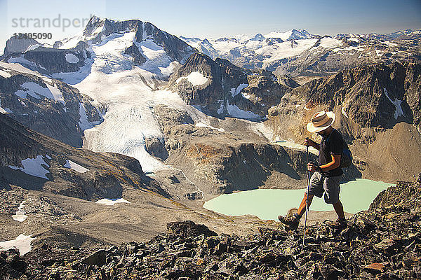 Ein Wanderer überquert einen felsigen Grat in der Nähe des Mount Cook mit Blick auf den Wedge Mountain und den Wedgemount Lake  der zum Garibaldi Provincial Park gehört  im Hintergrund.