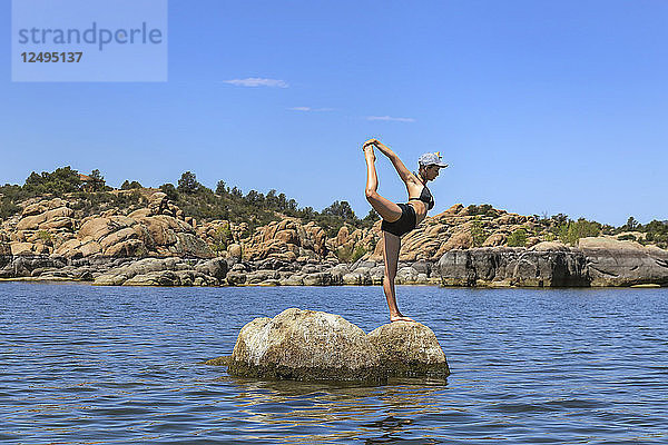 Ein sportliches Teenager-Mädchen posiert auf einem Felsen in einem See