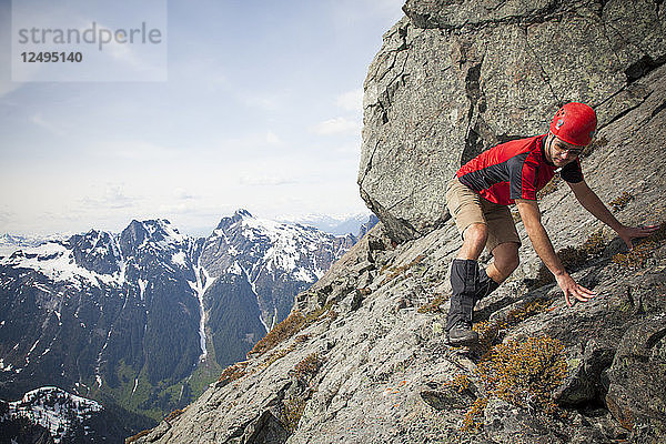 Ein Bergsteiger quert vorsichtig eine steile Felsplatte in der Nähe des Gipfels von Trio Peak  British Columbia  Kanada.