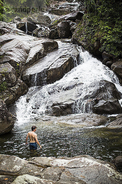 Ein junger Mann schwimmt in einem Pool am Fuße eines Wasserfalls in Puerto Rico