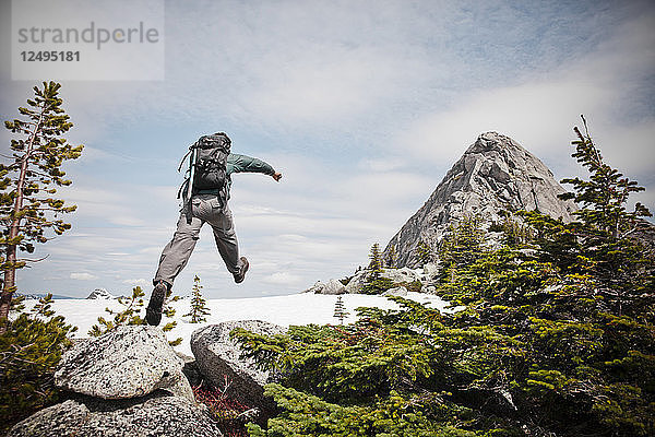 Ein Rucksacktourist springt auf ein Stück Schnee  während er sich dem Gipfel des Needle Peak nähert.