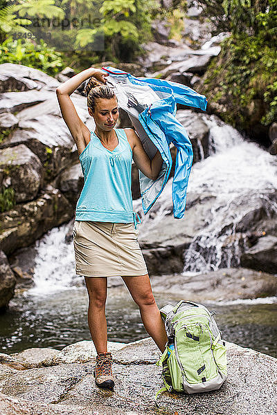 Frau trägt Jacke vor einem Wasserfall und Bach in einem Puerto Rico