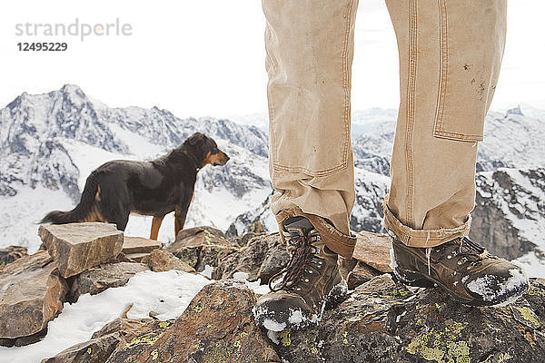 Ein Hund und die Beine und Stiefel eines Wanderers auf dem Gipfel des Frosty Mountain  British Columbia  Kanada.
