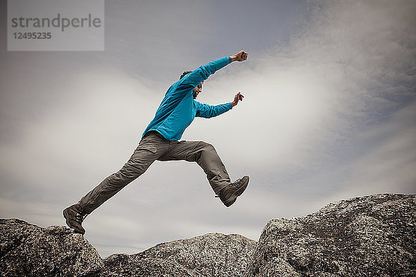 Ein Wanderer springt zwischen zwei Granitfelsen auf dem Gipfel des Needle Peak  BC  Kanada.