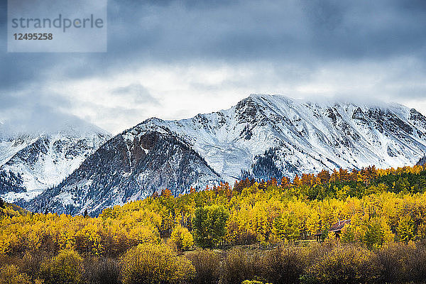 Erster Schneefall auf den Bergen mit Herbstfarben im Vordergrund