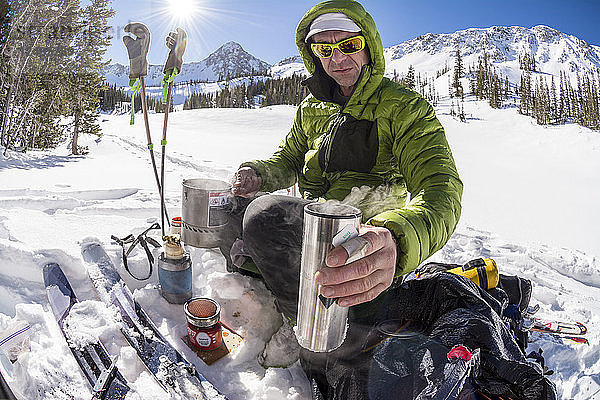 Ein Mann kocht heißen Tee während einer Skitour unterhalb des Pfeifferhorns im Little Cottonwood Canyon  Lone Peak Wilderness  Uinta-Wasatch-Cache National Forest  Salt Lake City  Utah.