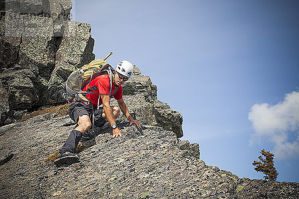 Ein Bergsteiger klettert vorsichtig einen felsigen Gipfel in British Columbia  Kanada  hinunter.
