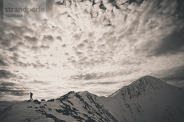 Ein Rucksacktourist und sein Hund wandern über einen felsigen Grat zum Gipfel des Frosty Mountain in der North Cascade Mountain Range.