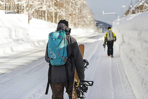Snowboarder zu Fuß entlang Schnee bedeckt Side Walk zum Resort in Niseko  Japan