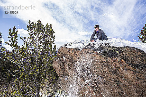 Männlicher Bergsteiger reinigt Schnee von einem Felsblock im Rocky Mountain National Park  Colorado